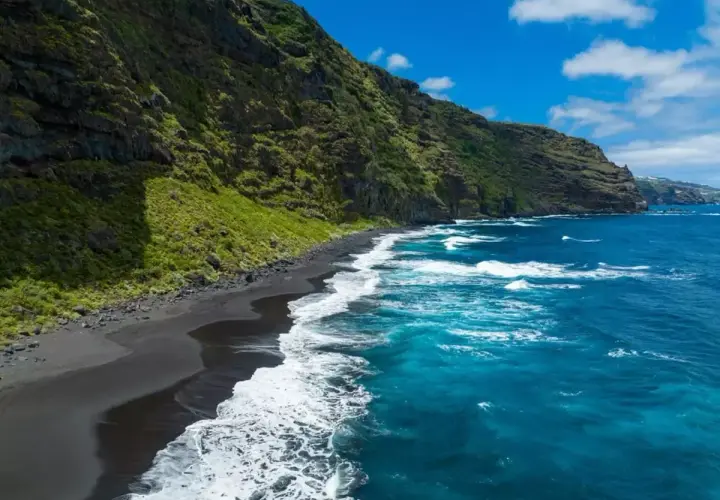 Costa salvaje con arena negra y mar azul intenso, un rincón idílico de las playas de Canarias.