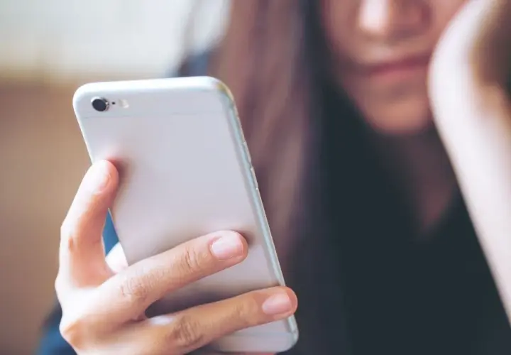Kobieta trzyma telefon, zastanawiając się, jak wysłać mms.