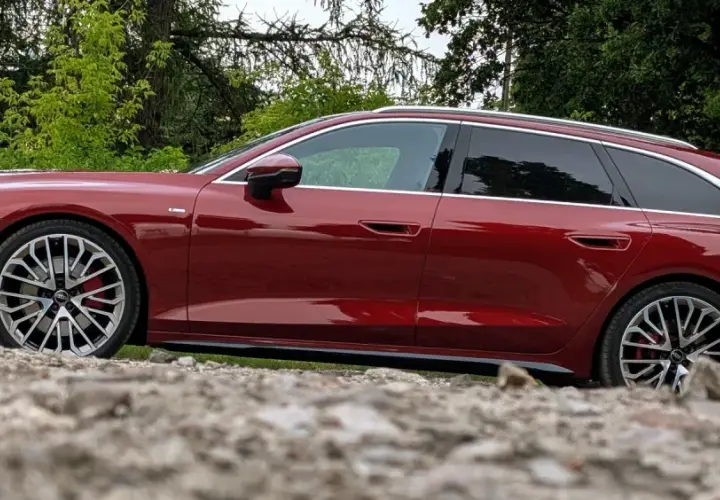 Lśniące, czerwone Audi A6 C9 Avant stoi na kamienistym podłożu, otoczone zielenią.