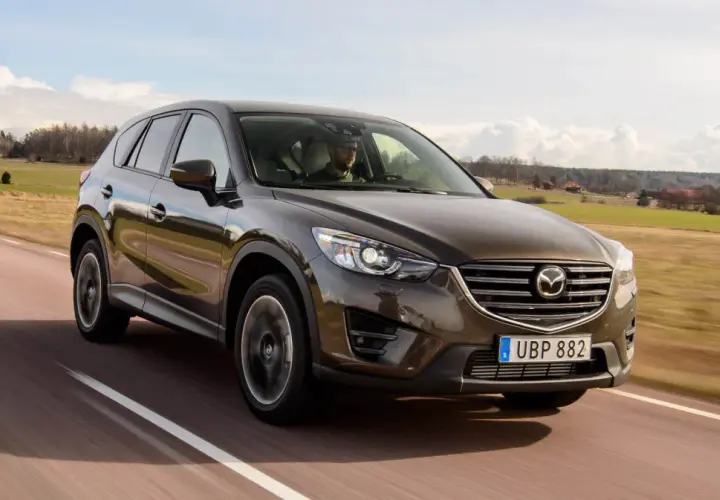 Brun Mazda CX-5 kör på en landsväg i Sverige. Föraren verkar ha ett problem med bilen.