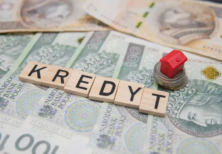 Kredyt 400 tys jaka rata? Mały czerwony domek na stosie monet i banknotów symbolizuje marzenie o własnym M.