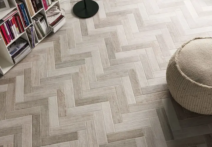Un elegante pavimento ruvido interno in parquet a spina di pesce, con una libreria e un pouf.