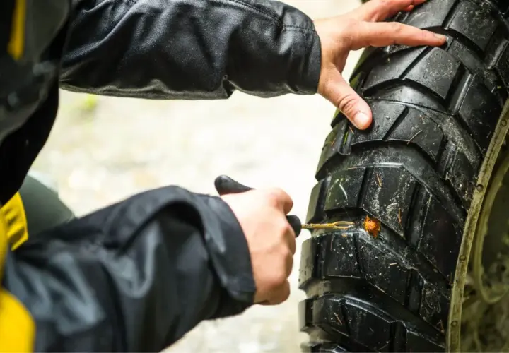 Manos arreglando pinchazo moto con kit de reparación.