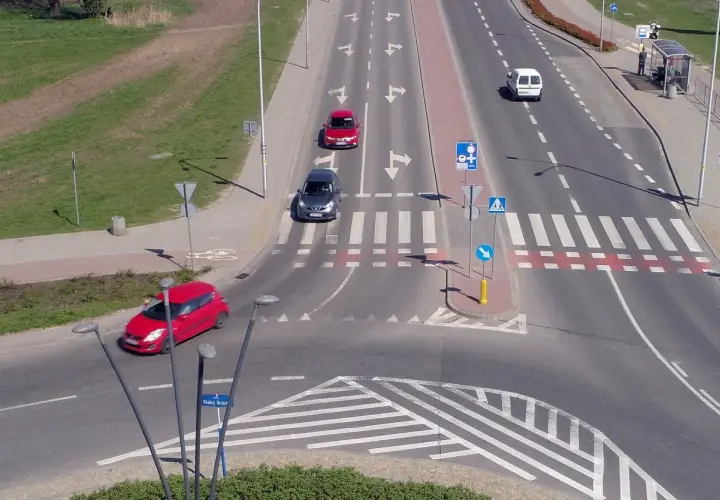 Samochody poruszają się po skrzyżowaniu z oznakowaniem sugerującym rondo turbinowe.