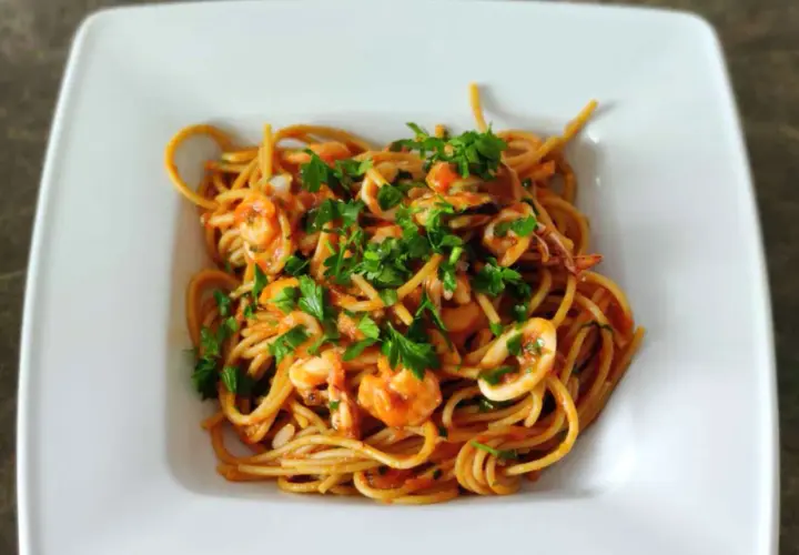 Pyszne spaghetti z owocami morza, krewetkami i kalmarami, posypane świeżą natką pietruszki.