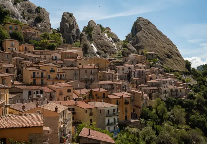 Houses cling to a mountainside in Pietrapertosa, Italy, beneath dramatic rock formations.