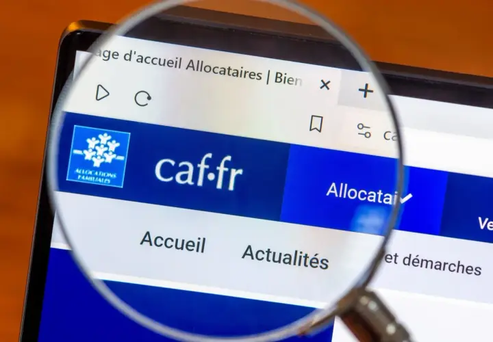 Loupe sur l'écran d'un ordinateur affichant le site caf.fr, page d'accueil des allocataires. L'accès aux informations est facilité.