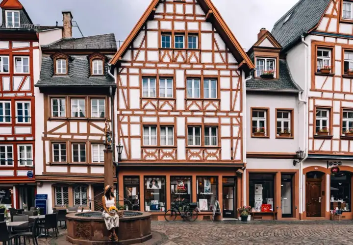Fachwerkhaus-Idylle in Mainz. Eine Frau sitzt am Brunnen, umgeben von malerischen Gassen – hier sind die echten Mainz Geheimtipps!