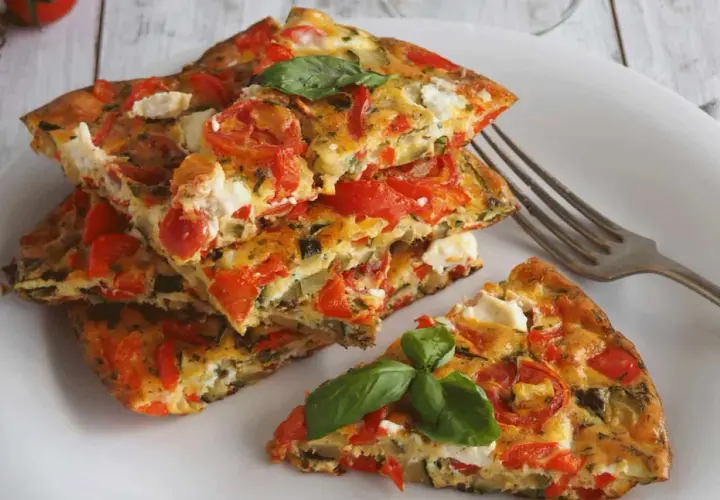 Une part d'omelette aux légumes colorée, garnie de tomates, courgettes et fromage frais, avec une feuille de basilic.