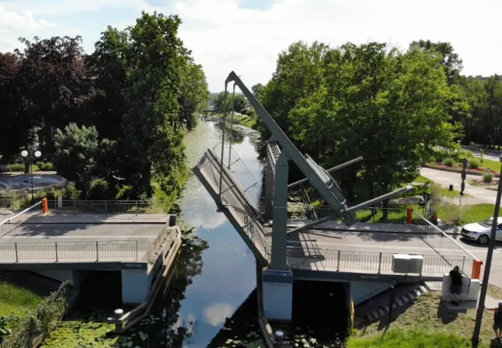 Podniesiony most zwodzony w Nowym Dworze Gdańskim, nad kanałem otoczonym zielenią.