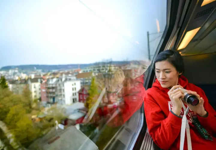 Joven en tren, con cámara, mirando el paisaje urbano. Quizás viajando en un tren de Tarragona a Sevilla.