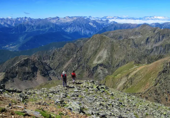 Dos excursionistas exploran las impresionantes **rutas de Esterri d'Àneu**, rodeados de picos montañosos y un cielo azul.