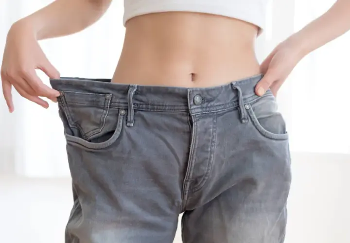 Une personne montre que j'ai perdu du poids en arrêtant de fumer, ses jeans sont trop grands.
