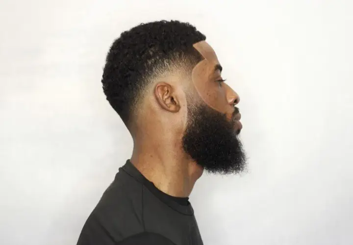 Hombre con barba tupida y corte de pelo con taper fade bajo, líneas definidas y degradado impecable.