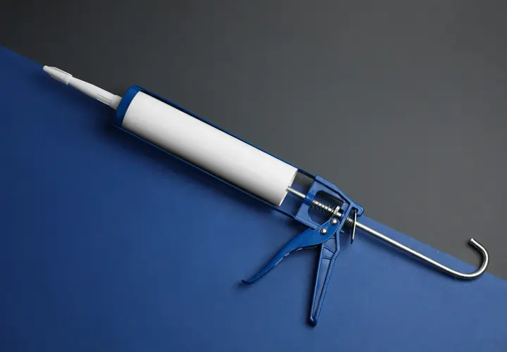 Niebieski pistolet do silikonu z białą tubą. Gotowy do pracy, gdy tylko pojawi się coś, co rozpuszcza silikon.