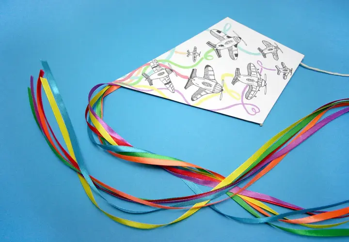 Kolorowy latawiec DIY z rysunkami samolotów i tęczowymi wstążkami.