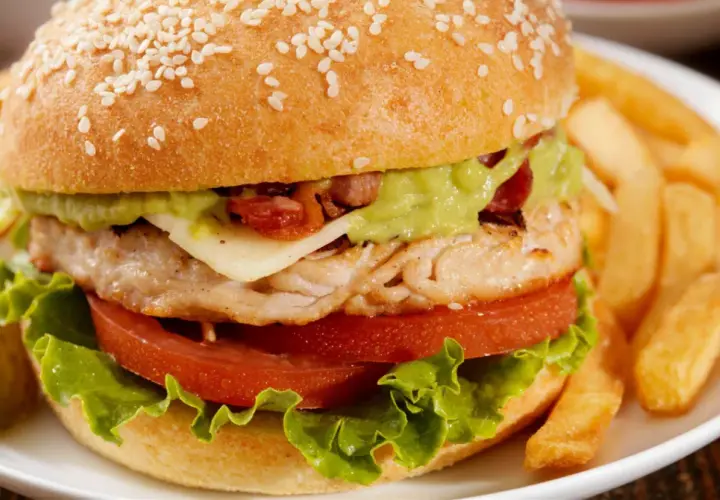 Pyszny burger z kurczakiem, z awokado, serem i chrupiącym bekonem, podany z frytkami.