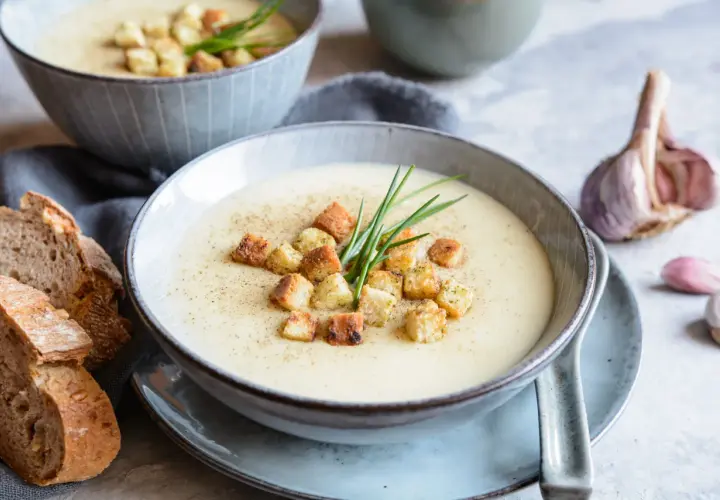 Aksamitna zupa czosnkowa z grzankami i szczypiorkiem, podana z chlebem i czosnkiem.