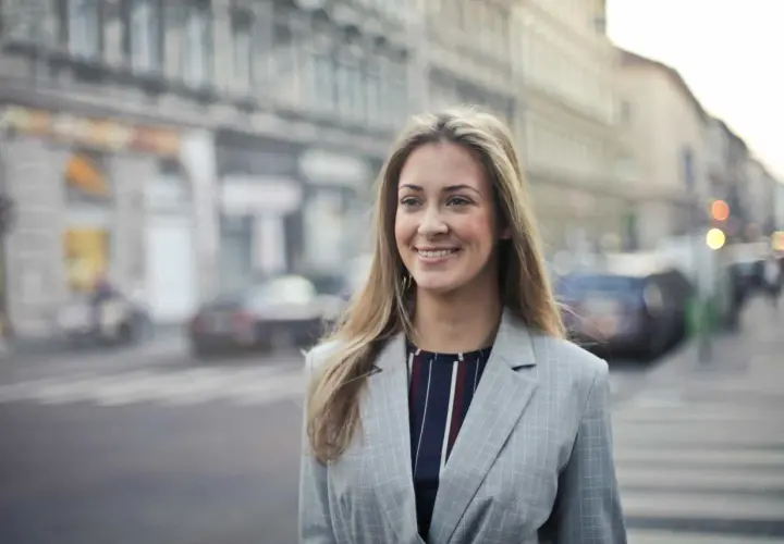 Uśmiechnięta kobieta w marynarce na tle miasta. Czytała pozytywne renee opinie forum i postanowiła wybrać się na spacer.