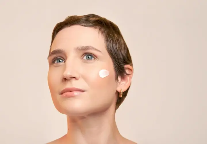 Visage d'une femme avec une touche de crème sur la joue, évoquant la protection contre le soleil pendant une hormonothérapie.