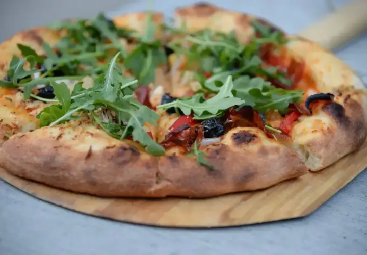 Pyszne ciasto na pizzę z rukolą, oliwkami i papryką, podane na drewnianej desce.