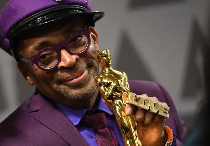 Spike Lee, w fioletowym garniturze i czapce, trzyma Oscara z napisem "LOVE". Jego filmy często poruszają ważne tematy społeczne.