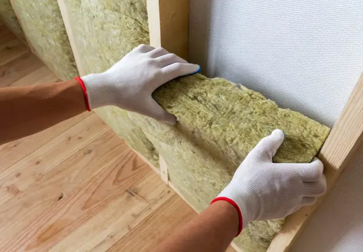 Mains gantées installant un isolant minéral dans une structure en bois pour une isolation intérieure efficace.