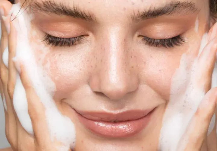 Une femme se nettoie le visage avec de la mousse. Un geste simple pour un teint frais, découvrez comment nettoyer son visage pour une peau éclatante.