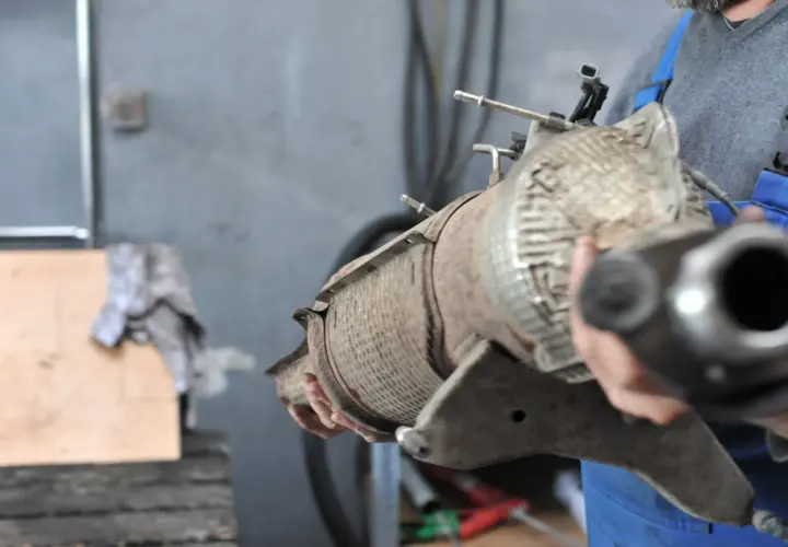 Mechanik trzyma zużyty filtr DPF w warsztacie samochodowym.