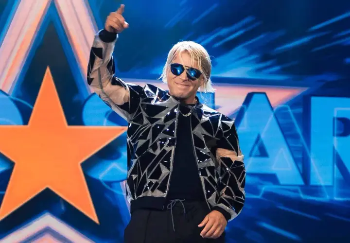 Skolim w błyszczącej kurtce i okularach przeciwsłonecznych pozdrawia publiczność na tle sceny z napisem "STAR".