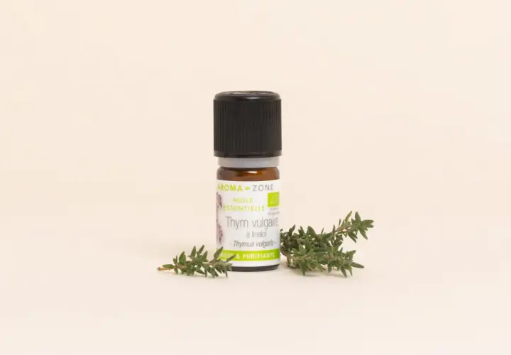 Flacon d'huile essentielle de thym vulgaire, aux notes aromatiques et purifiantes, posé à côté de brins de thym frais.