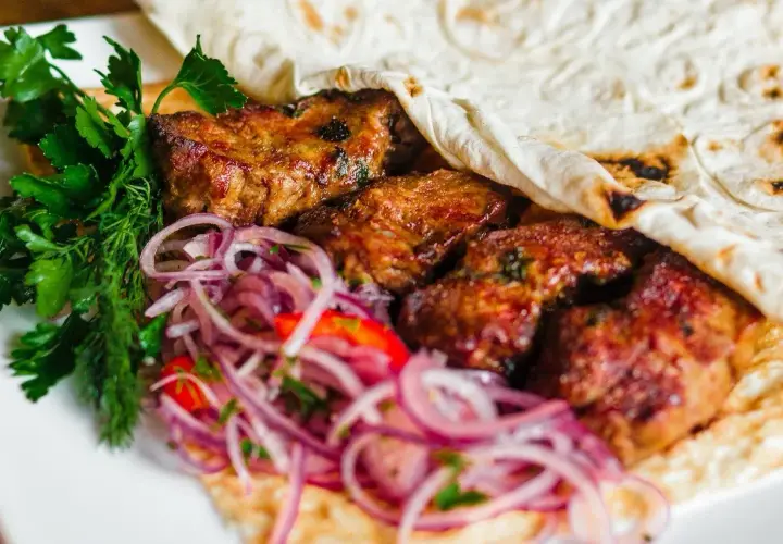Soczyste mięso kebab zawinięte w placek, podane z czerwoną cebulą i świeżą natką pietruszki.