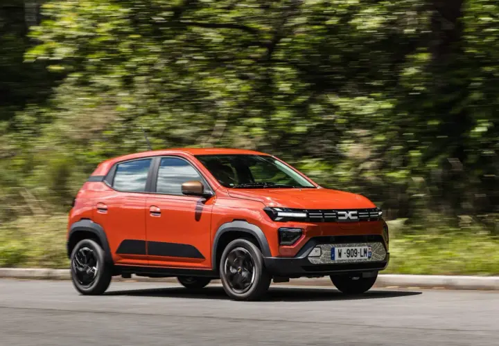 Auto arancione in movimento, con cambio automatico, su strada circondata da alberi sfocati.