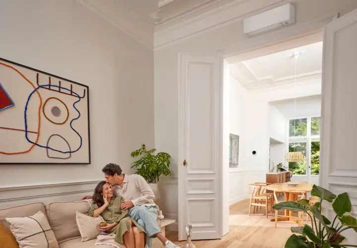 Pareja feliz en un salón moderno. El aire acondicionado Daikin, símbolo de calor confortable, se ve en la pared.