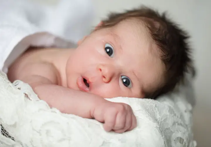 Un neonato con occhi spalancati, che sembra scoprire il mondo. La sua espressione curiosa cattura il momento in cui iniziano a vedere i neonati.