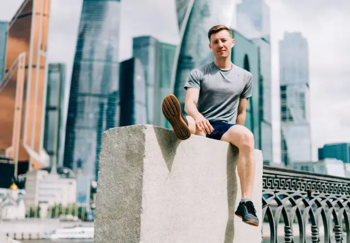 Mężczyzna w sportowym stroju siedzi na kamiennym postumencie, w tle nowoczesne wieżowce. Czasem czuję, że nie mogę złapać oddechu podczas biegania.
