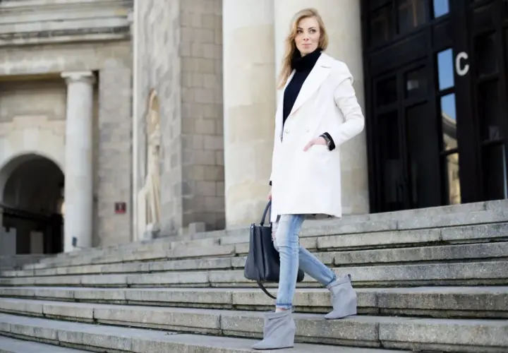 Elegancka kobieta w białym płaszczu i jeansach schodzi po schodach. Stylowe biały płaszcz stylizacje na co dzień.