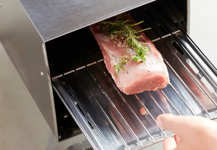 Un filet de porc fumé, assaisonné d'herbes et de poivre, est placé sur une grille dans un fumoir en acier inoxydable.