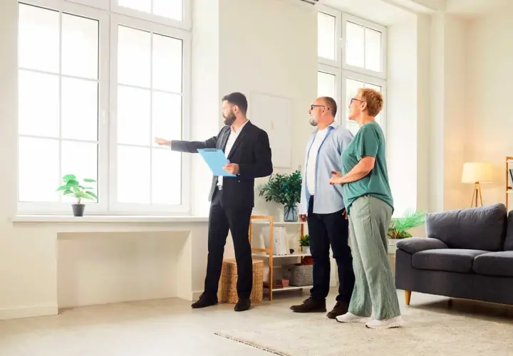 Agente inmobiliario explica a pareja cuánto dura una tasación, señalando la luz natural de la vivienda.