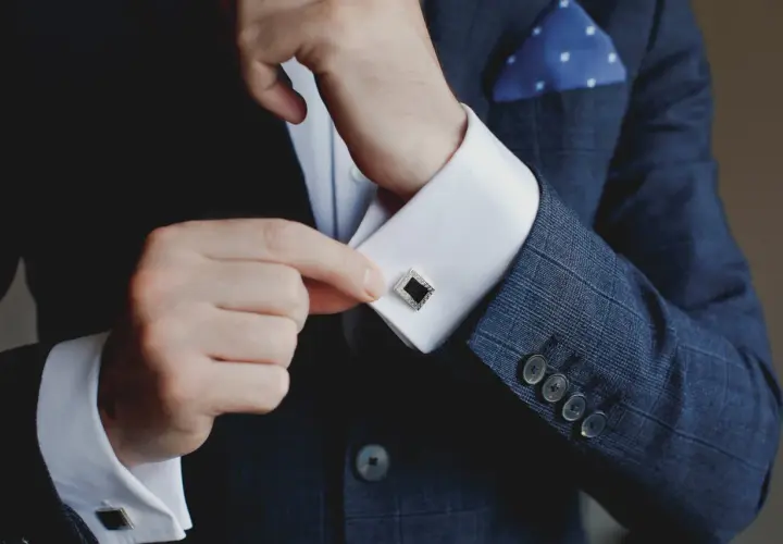 Mann schließt Manschettenknöpfe an seinem Hemd. Was ist eine Manschette? Ein elegantes Accessoire, das den Hemdsärmel verschließt und Stil verleiht.