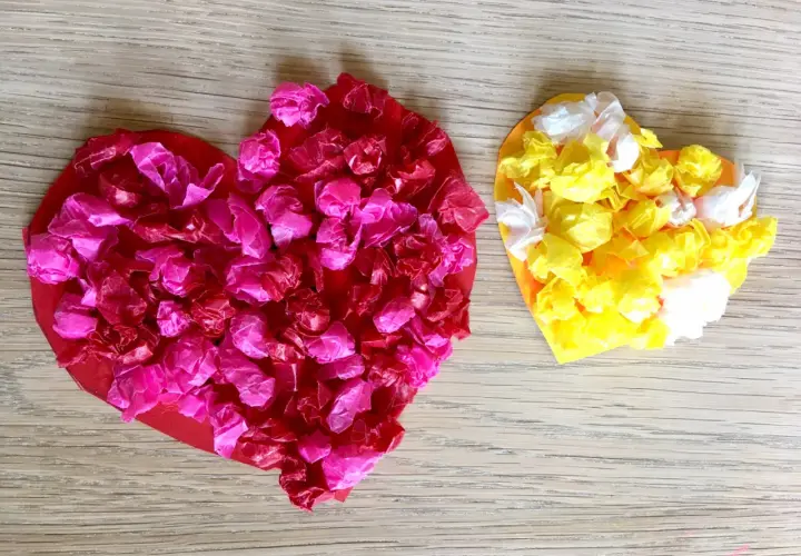 Zwei bunte Herzen, rot und gelb, mit zerknülltem Seidenpapier beklebt. Ein schönes Beispiel für herz basteln kinder.