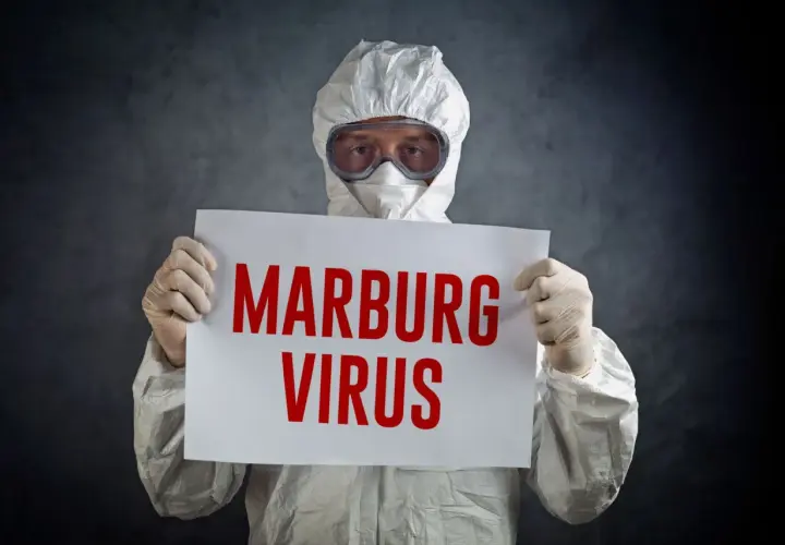 Osoba w kombinezonie ochronnym trzyma tabliczkę z napisem "MARBURG VIRUS".