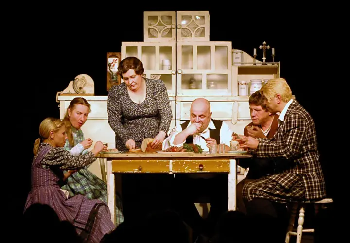Scena z życia rodzinnego na stole obficie zastawionym jedzeniem. Sprawdź teatr Korez repertuar, by zobaczyć więcej takich przedstawień.