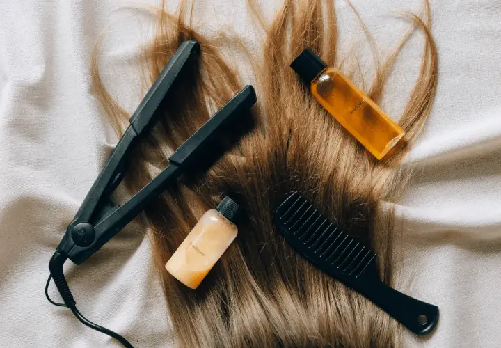 Plancha, peine y botellitas de champú y acondicionador sobre cabello rubio. Una solución casera para el pelo naranja.