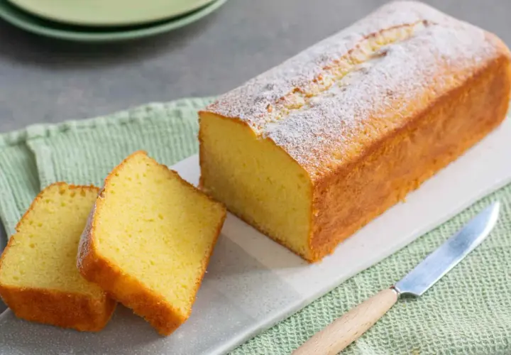 Un soffice plumcake yogurt, spolverato di zucchero a velo, pronto per essere gustato. Due fette sono già state tagliate.