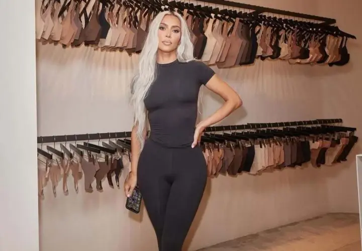 Kim Kardashian w czarnym dopasowanym stroju, na tle wieszaków z bielizną. Skims w Polsce gdzie kupić? Sprawdź ofertę!