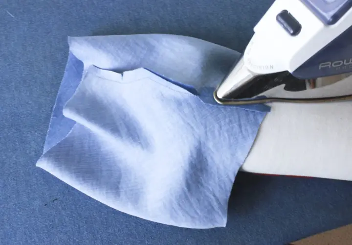 Ironing a folded cuff band to a light blue sleeve. This step is crucial for how to sew a folded cuff band to a sleeve.