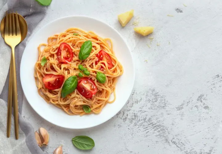 Leckere Tagliatelle Rezepte: Spaghetti mit Tomaten, Basilikum und Parmesan auf einem Teller, daneben goldene Gabel und Messer.