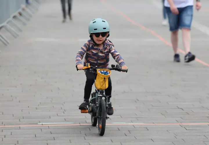 Małe dziecko w kasku i okularach przeciwsłonecznych śmiga na rowerze, wyciągając język. To dziecko na rowerze przepisy, jak prawdziwy mistrz.