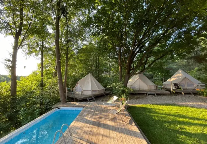 Luksusowy glamping nad jeziorem: namioty tipi na drewnianych tarasach, basen i leżaki wśród drzew. Idealne miejsce na relaks.